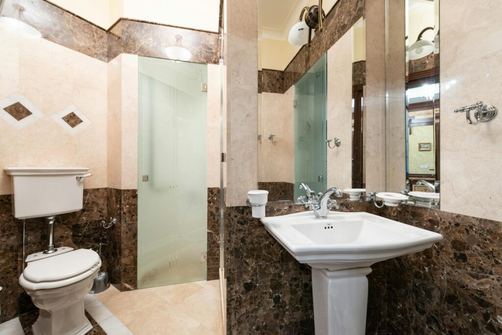 A contemporary bathroom featuring brown marble tiles, glass shower door, and classic fixtures.